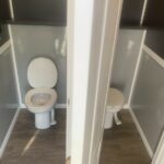 image displays the interior of a two-stall portable toilet unit, commonly known as a mobile toilet or portable restroom